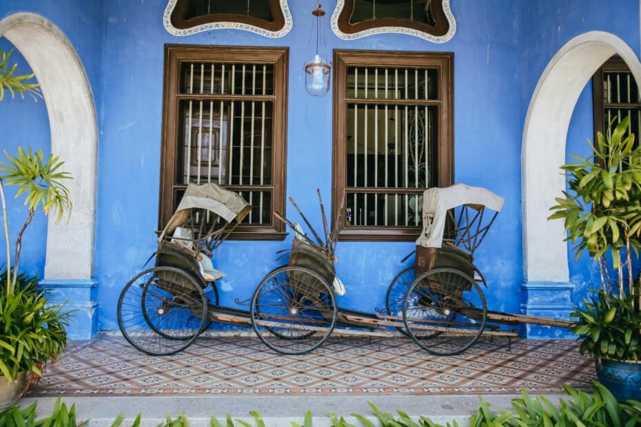 Two vintage rickshaws rest against a vibrant blue wall in George Town, Malaysia.